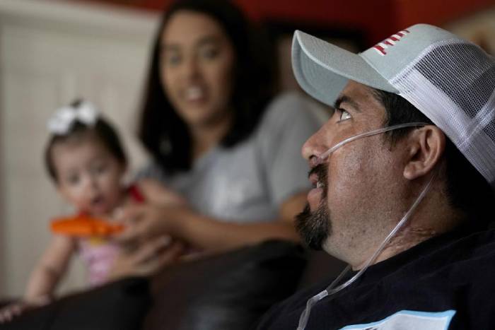 Freddy Fernandez se sienta con su prometida, Vanessa Cruz, y su hija de ocho años, Mariana Fernández, en su casa del viernes 10 de junio de 2022, en Carthague, Missouri. Freddy Fernández, de 41 años y que tiene seis hijos, pasó cinco meses hospitalizado a cuatro horas de carretera de su casa en Carthage, en el suroeste de Missouri, y estuvo sujeto al sistema más intensivo de soporte vital que había disponible. Estuvo a punto de morir en varias ocasiones, y ahora, como muchos de los que sobrevivieron a hospitalizaciones por COVID-19, ha vuelto cambiado. (AP Foto/Charlie Riedel)